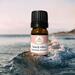 Bottle of Beach Vibes Essential Oil Blend by Whole Self Aromatherapy sitting in water with a small ocean wave splashing against it.